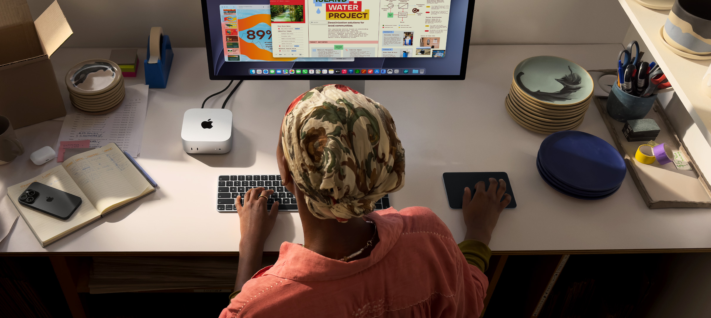 Una persona escribe en un escritorio que tiene una Mac mini, un monitor Studio Display conectado, un Magic Keyboard, un Magic Trackpad, varios artículos