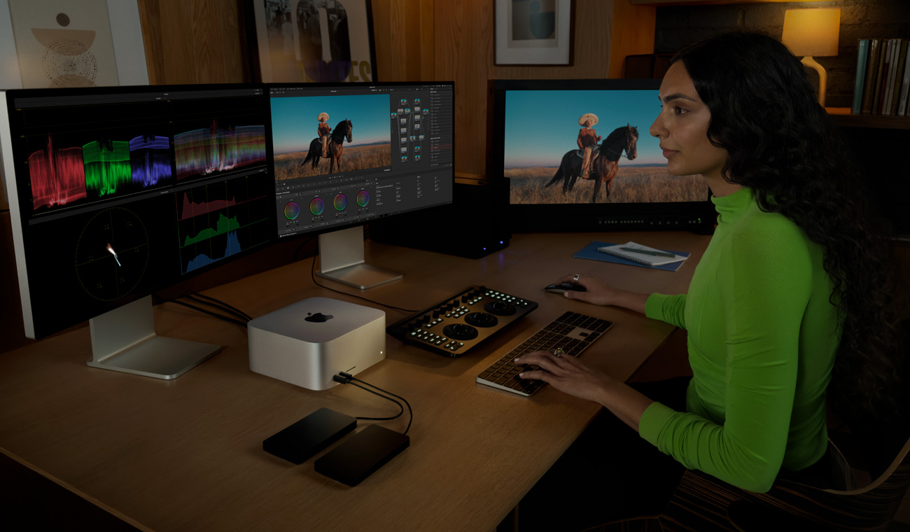 一位專業人士使用已連接三部顯示器的 Mac Studio 編輯檔案