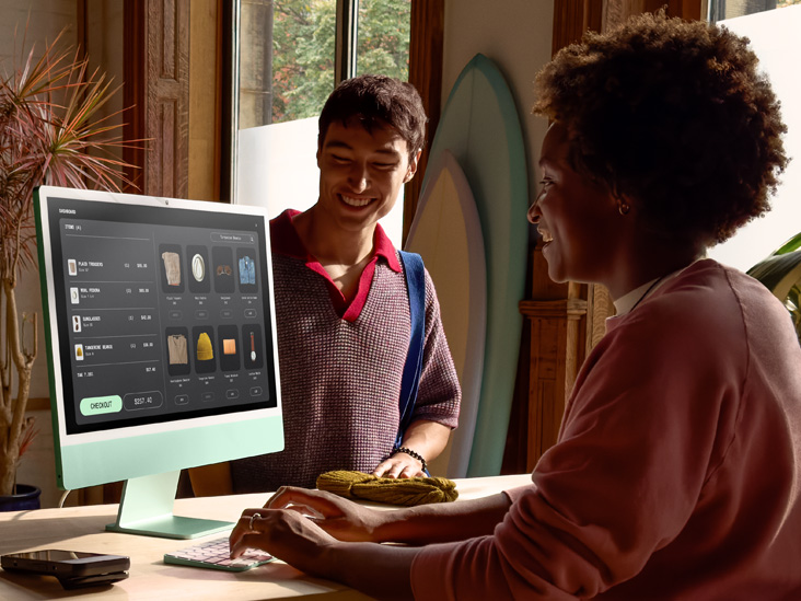 Dos personas en una estancia bien iluminada. Una de ellas revisa un pedido en un iMac con chip M4 en verde.
