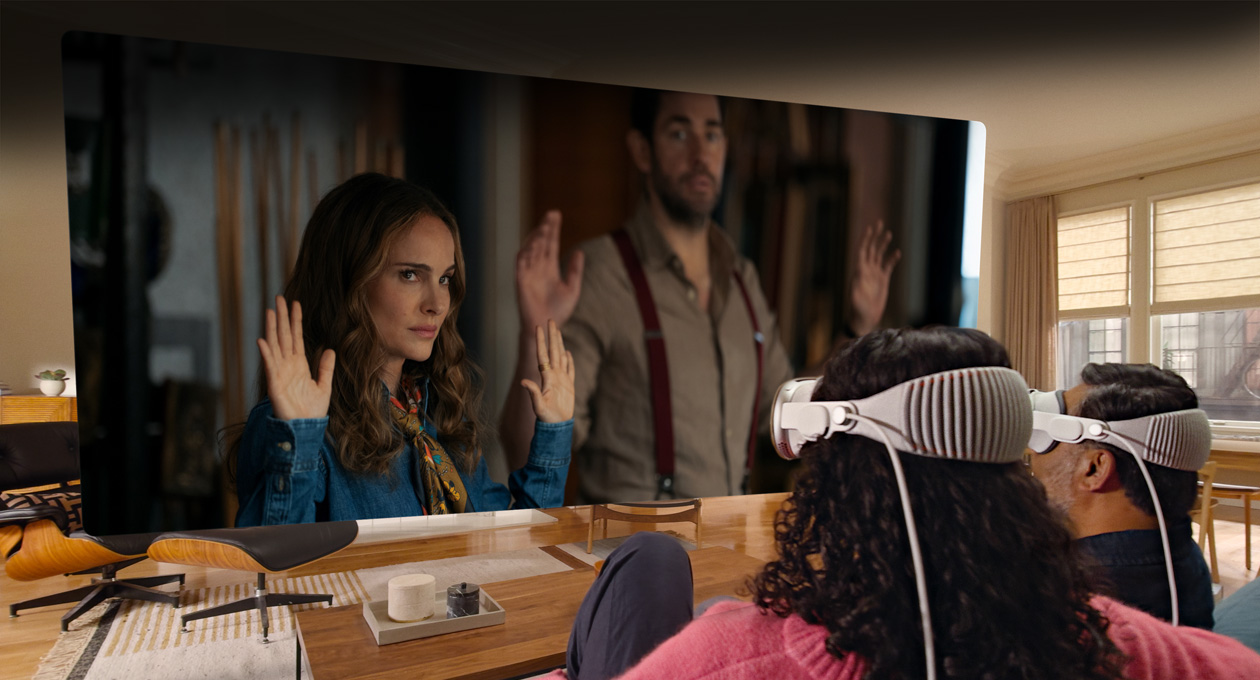 Two people both wearing Apple Vision Pro sit side by side on sofa watching Fountain of Youth movie, displayed on screen stretching across room