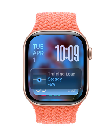 Ruusukullan värinen Apple Watch ja punottu mandariininoranssi ranneke, kellotaulun vasemmassa yläkulmassa näkyy päivämäärä, oikeassa yläkulmassa näkyvissä numerot päällekkäin, Treenikuorma-widgetti alhaalla, kaikki läpikuultavalla Liquid Glass ‑käyttöliittymällä