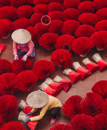 Foto de dos personas secando manojos de incienso de color rojo brillante