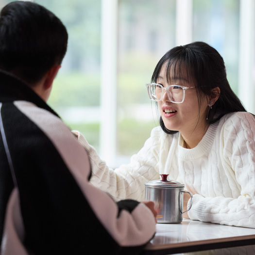カフェテリアのテーブルで、2人の人物が向かい合って話をしている