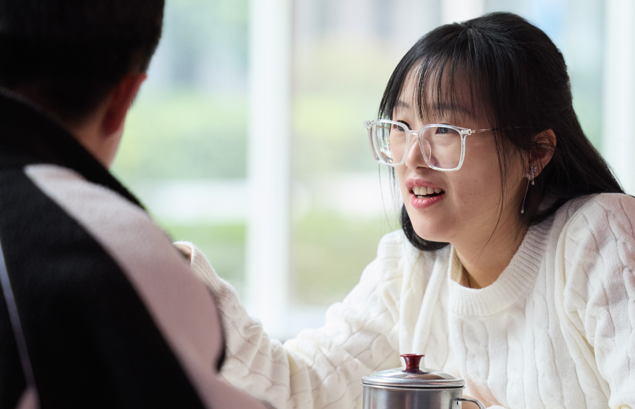 カフェテリアのテーブルで、2人の人物が向かい合って話をしている
